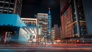 夜晚的城市街道，有明亮的建築物和移動車輛的光軌。