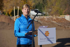 藍色外套女性在建築工地講台發言，帶有Solar Forma標誌。 — 政治 壁紙