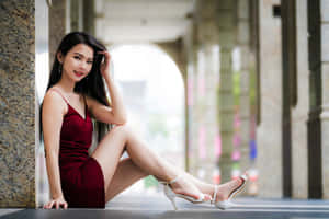 身穿紅色連衣裙和白色高跟鞋的女性靠在拱廊的石柱上。