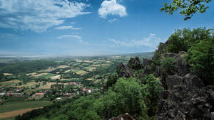 從岩石懸崖俯瞰的 panoramic 景觀，綠色山谷中有田野和村莊。