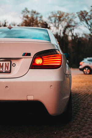 白色BMW M車的發光尾燈，停在黃昏時的鵝卵石路上。