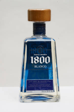一個1800 Blanco龍舌蘭酒瓶，帶有藍色標籤和木蓋，放在白色表面上。