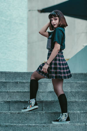身穿格仔裙和魚網絲襪的年輕女性在混凝土階梯上擺姿勢。