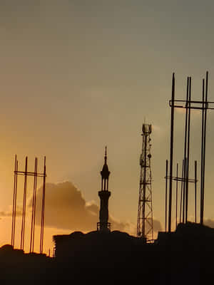 宣禮塔和塔樓在金色夕陽下的剪影，前景有建築鋼筋