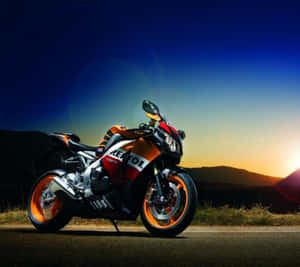 一輛 Repsol 電單車在日落時停泊在道路上，背景是山丘。 — 機車 壁紙