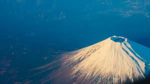 日出時白雪覆蓋的富士山，下方是藍色海洋和森林覆蓋的山谷。