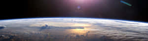 日出時從太空看地球，雲層和海洋在金色光芒中閃耀。 — 32:9 壁紙