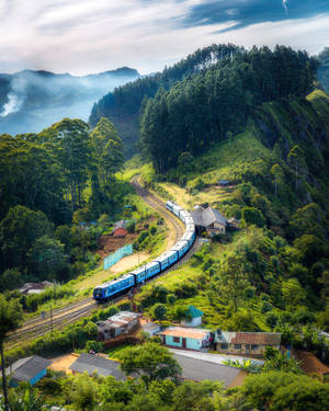 藍色火車在綠色山區地形中彎曲行駛，靠近一個小村莊。
