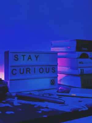 一個寫著「STAY CURIOUS」的燈箱，旁邊有書籍和一支筆，桌上濺滿油漆，在霓虹光下。
