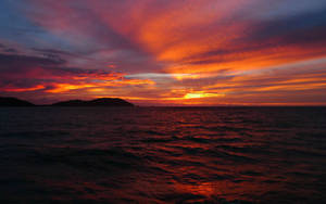 海洋上戲劇性的夕陽，剪影島嶼和熾熱的紅橙色天空。