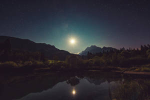 月光倒映在被山脈和樹木環繞的湖面上，星空下。
