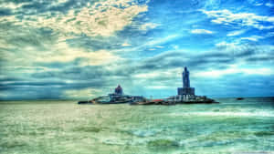 在多雲的天空下，海中的岩石島上矗立著一座高聳的雕像和寺廟。