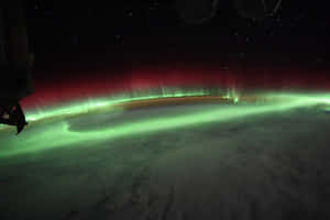 極光從太空在地球上空發出綠色和紅色的光芒，背景有星星。 — 月色夜空 壁紙