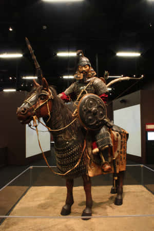 博物館展示櫃中全副武裝、手持弓和盾牌的騎馬戰士雕像。 — Huawei MatePad Pro Max 壁紙