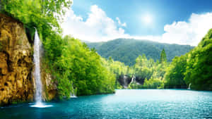 瀑布流入一個碧綠色的湖泊，周圍是茂密的綠色森林和山丘。 — 桌面美學 壁紙