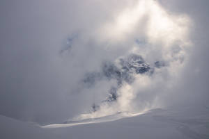 積雪的山峰穿破雲層，前景有滑雪痕跡。