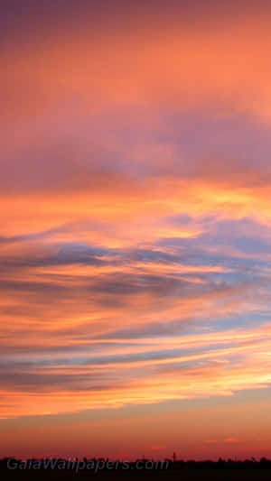 充滿活力的日落天空，橙色、粉紅色和紫色雲彩在黑暗的地平線上方。