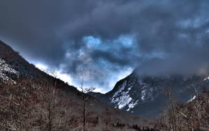 冬季山脈，有雪和光禿禿的樹木，在暴風雨的天空下，帶有藍色斑塊。