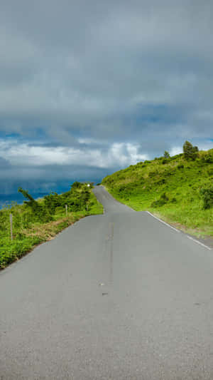蜿蜒的道路穿過綠色山丘，多雲的天空，遠處有海洋 — 夏威夷 壁紙