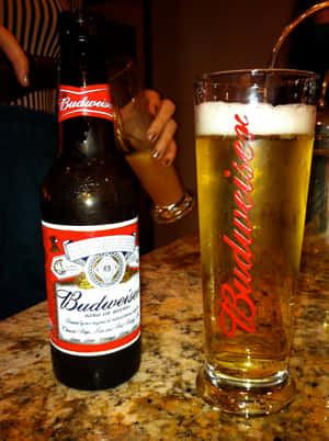 冰凍的Budweiser啤酒瓶和玻璃杯放在大理石酒吧上，有一隻手拿著另一個玻璃杯。 — iPad Pro M4 壁紙