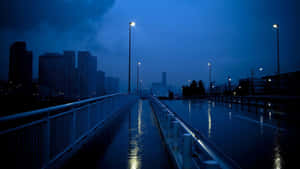 暮色中雨水浸濕的城市橋樑，閃爍的街燈和背景中黑暗的摩天大樓。 — 昏暗 壁紙