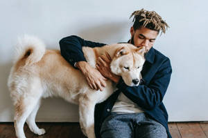 留著辮子頭的男子在室內擁抱一隻柴犬。