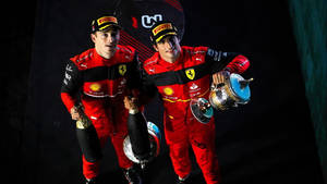兩名身穿紅色賽車服的F1車手在夜間手持獎盃和香檳瓶。