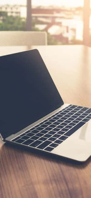 銀色手提電腦放在木桌上，陽光從窗戶照進來