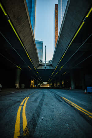 空蕩的城市高速公路地下通道，帶有黃色標線和摩天大樓，在暮色天空下
