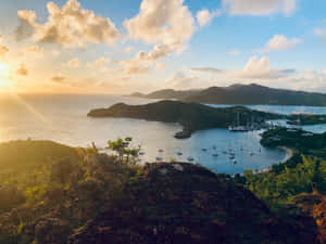 帆船在夕陽下停泊於熱帶海灣，伴隨著金色光芒和綠色山丘。 — 熱帶海灘 壁紙