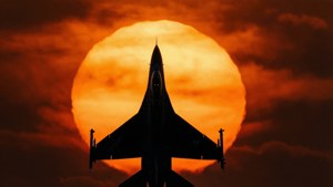 戰鬥機在帶有橙色雲彩的夕陽前飛行。