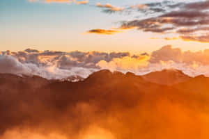 沐浴在金色夕陽下的山脈，下方有雲和薄霧。 — 夏日氣息 壁紙