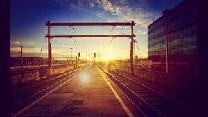 夕陽下的空火車軌道，背景是現代玻璃建築 — 日出 壁紙
