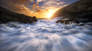 夕陽的光線照亮了黑暗懸崖之間拍打的海浪。 — 5120x2880 壁紙