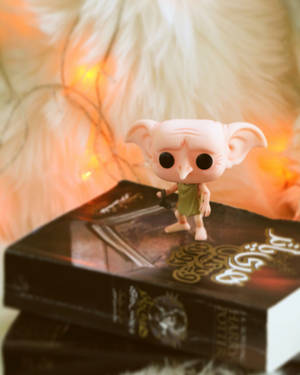 多比 Funko Pop 人偶放在哈利波特書籍上，背景有仙女燈。