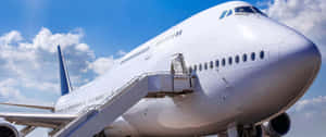 一架白色商用飛機帶有登機梯，在晴朗藍天白雲下。 — 雲朵 壁紙