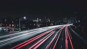 夜間高速公路，車燈流線通向城市天際線。