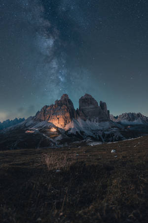 崎嶇山脈上方的星空夜空，下方有溫暖的燈光。