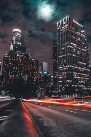夜晚的城市，有發光的建築物和移動汽車的紅色光跡。 — 夜晚 GIF 壁紙