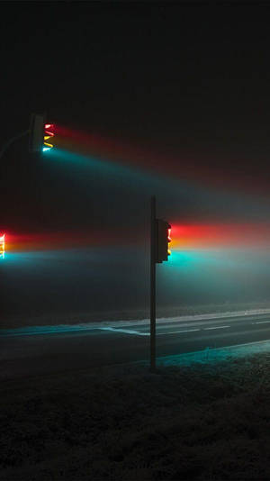 有霧的夜晚場景，發光的交通燈在荒蕪的道路上投射出色彩繽紛的光束。 — 夜晚 GIF 壁紙