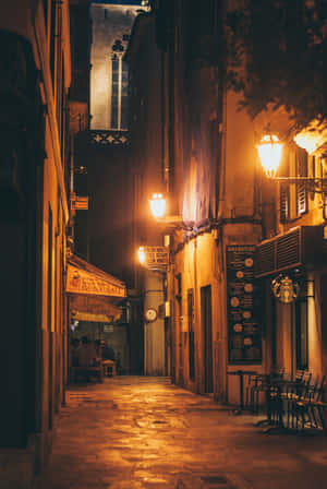 夜晚狹窄的鵝卵石小巷，被溫暖的街燈和咖啡館招牌照亮。 — 夜景城市 壁紙