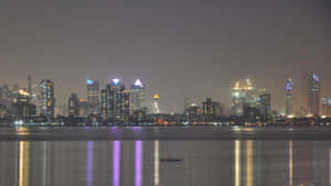 夜晚城市天際線，發光的建築物倒映在平靜的水面上，還有一艘小船。 — 夜景城市 壁紙
