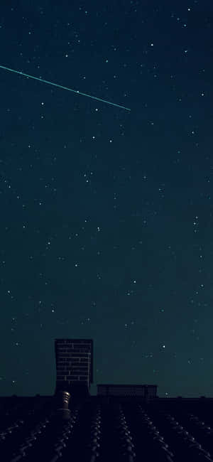 星空下屋頂的剪影，一顆流星劃過天空。 — iPhone 16 壁紙