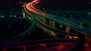 夜晚高速公路，有車燈光軌和模糊的城市建築。 — 夜晚 GIF 壁紙