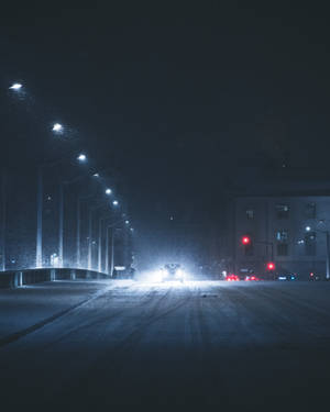 積雪的夜晚街道，有車頭燈和紅色交通燈。