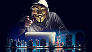 戴面具的駭客在夜晚發光的城市天際線前指向筆記型電腦。