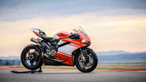 日落時分賽道上的紅白色 Ducati 電單車，背景有山。