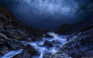 岩石海岸線上的星空夜空，帶有發光的藍色海洋波浪。