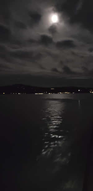 月光在水面上反射，遠處的城市燈光在多雲的夜空下 — 夜晚 GIF 壁紙