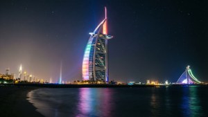 帆船酒店在夜間被彩色燈光照亮，在星空下的水面上反射